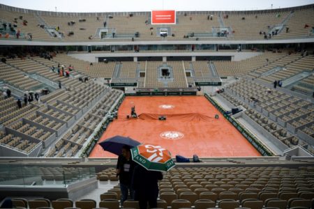 Dos personas con sendos paraguas abandonan las gradas del estadio de tenis bajo la lluvia que obligó a suspender la jornada del torneo de Roland Garros